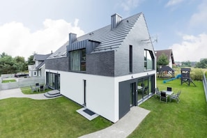 A modern two-story house with a sloped roof, large windows, and a visible play area with a slide.