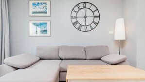Ein modernes Wohnzimmer mit einem grauen Sofa, einem Holztisch und einer Wanduhr.