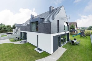 A modern two-story house with a flat roof, large windows, and a well-maintained lawn.