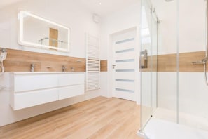 A modern bathroom with a wooden vanity, a large mirror, and a glass shower enclosure.