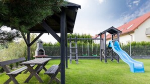 Ein Spielplatz mit Rutsche, Schaukeln, einem Picknicktisch und einem Grill.