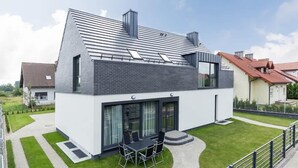 Ein modernes, zweistöckiges Haus mit Satteldach, großen Fenstern und einer Terrasse mit Gartenmöbeln.