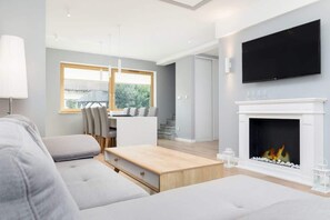 A modern living room with a fireplace, a flat-screen TV, and a dining area with a table and chairs.
