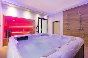 A modern spa room with a hot tub, a steam room, and a shower area.