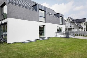 A modern two-story house with a white facade and grey roof, featuring large windows and a small front yard.