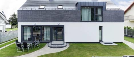 A modern two-story house with a flat roof, large windows, and a well-maintained lawn.