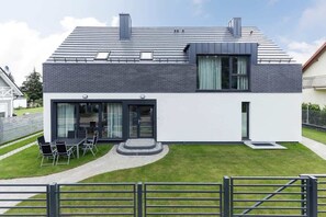 A modern two-story house with a flat roof, large windows, and a well-maintained lawn.