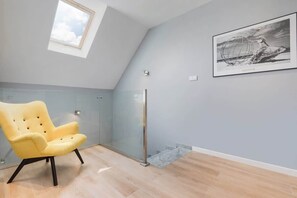 A modern room with a skylight, a glass partition, a yellow armchair, a framed artwork, and a glass door.