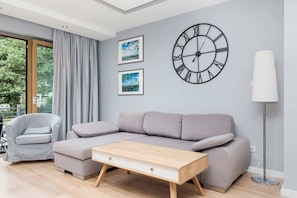 Un salon moderne avec un canapé gris, une table basse en bois, une lampe sur pied et une horloge murale.