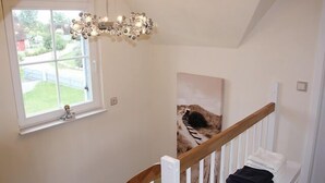 Een kamer met een raam, een kroonluchter, een schilderij en een trap.