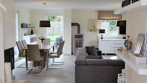 Een moderne woonkamer met een grijze bank, een eethoek met stoelen en een keuken met een fornuis en kasten.