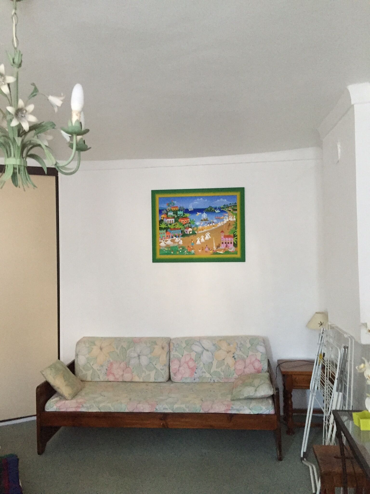A living room with a floral sofa, a hanging light fixture, and a framed painting on the wall.