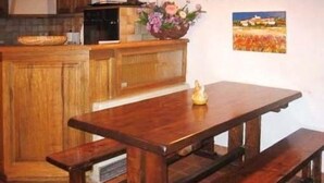A wooden table with benches in a kitchen area with a wooden cabinet and a flower vase.