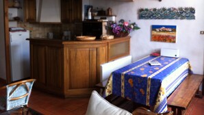A kitchen with wooden cabinets, a microwave, and a sink. There is a dining table with a blue tablecloth and a bench.