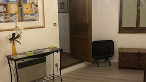 A room with a wooden floor, a black chair, a wooden cabinet, a framed painting, and a chandelier.