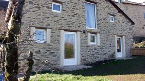 A stone building with a sloped roof, multiple windows, and a door. - Cottage of the Barry fountain in Aveyron (Le Vibal)