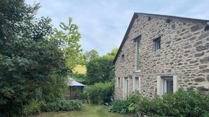 A stone building with a garden, a wooden fence, and a green watering can. - Cottage of the Barry fountain in Aveyron (Le Vibal)