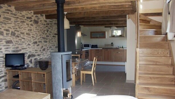 A cozy living room with a stone wall, a fireplace, a television, and a wooden staircase. - Cottage of the Barry fountain in Aveyron (Le Vibal)