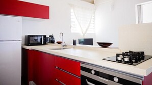 Una cocina con refrigerador blanco, microondas, estufa a gas y armarios rojos.