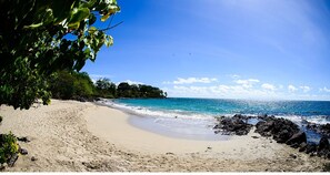 A beach with clear blue water, sandy shore, and some rocks near the water. - La Villa Diamant - Luxury on the waterfront - Pte La Cherry (le diamant)