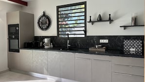 Une cuisine moderne dotée d’appareils électroménagers intégrés, d’une grande fenêtre avec stores et d’une horloge décorative.