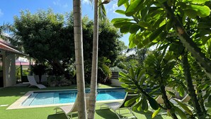 Une piscine entourée de gazon synthétique, avec des chaises longues et un palmier.