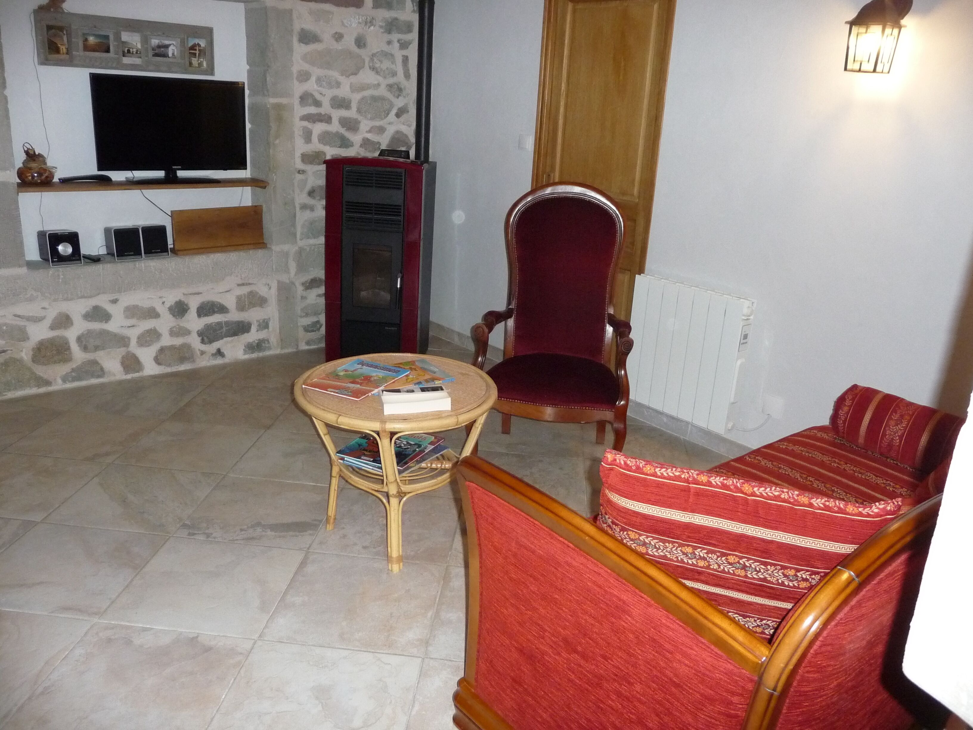 A living room with a television, a stone wall, a red chair, a round table with books, and a red sofa.