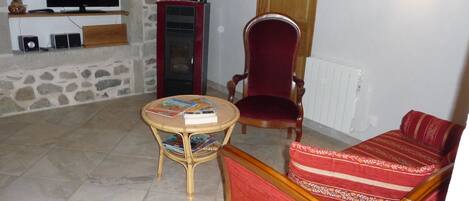 A living room with a television, a stone wall, a red chair, a round table with books, and a red sofa.