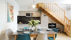 A modern kitchen with wooden cabinets, a dining area with a wooden table set for four, and a wooden staircase.