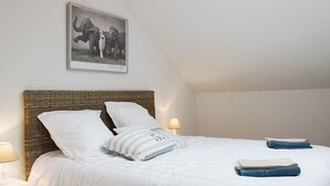 A bedroom with a bed, a nightstand, a lamp, a wall-mounted picture, and a skylight.