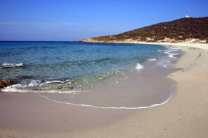 A beach with clear blue water, sandy shore, and a hill with sparse vegetation. - Marine of Sant'Ambroggio apartment in house (Lumio)