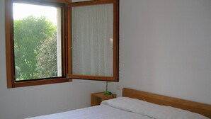Een slaapkamer met een bed, een raam met houten kader en een wandlamp.