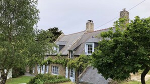 A stone house with a sloped roof, white shutters, and a small garden area with a bench. - Charming Small Farmhouse 600 M FROM THE BEACHES  (Cancale)
