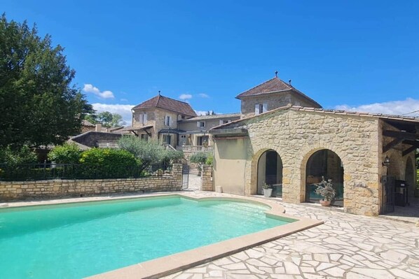 A pool area with a stone building, a stone wall, and a clear blue sky.
