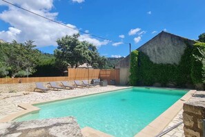 A swimming pool with lounge chairs, a stone deck, and a wooden fence.