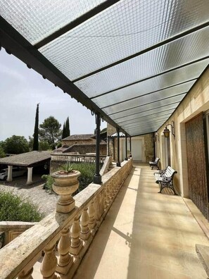 Um corredor externo coberto com pérgola, bancos e balaústres de pedra.