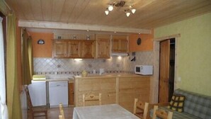 A compact kitchen with wooden cabinets, a microwave, and a dining area with a table and chairs. - 1st floor apartment in Savoyard chalet in Morzine. (Morzine)