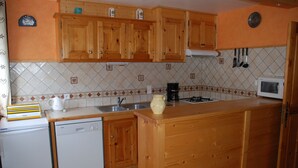 A kitchen with wooden cabinets, a dishwasher, a microwave, and a coffee maker. - 1st floor apartment in Savoyard chalet in Morzine. (Morzine)