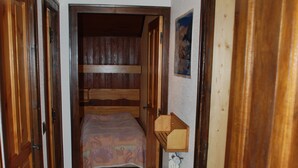 A narrow hallway with wooden doors on either side, leading to a room with a bed and a small wooden cabinet. - 1st floor apartment in Savoyard chalet in Morzine. (Morzine)