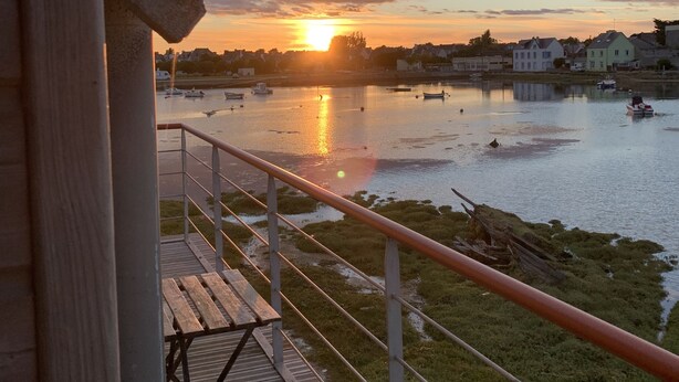 A wooden deck with a railing overlooking a body of water with boats, a sunset, and buildings in the background. -  Fisherman's house with exceptional view of the back port, close to the beaches (Treffiagat)