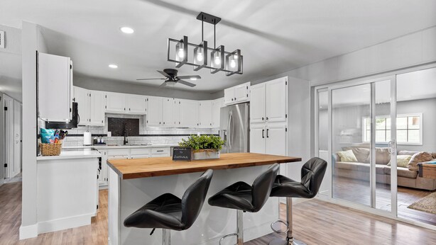 A modern kitchen with white cabinets, a wooden island with bar stools, a ceiling fan, and a view to a living area through glass doors. - Old Town Scottsdale - With a pool, hot tub,  Putting Green, Billiards. (Scottsdale)