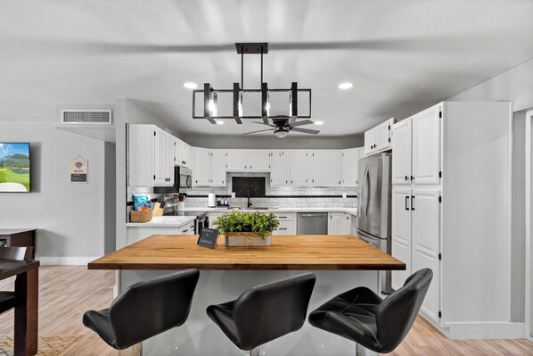 A modern kitchen with white cabinets, a wooden island with chairs, a ceiling fan, and a built-in TV. - Old Town Scottsdale - With a pool, hot tub, Putting Green, Billiards. (Scottsdale)