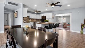 A spacious dining area with a long table and chairs, a kitchen with white cabinets and a stone backsplash, and a ceiling fan. - Old Town Scottsdale - With a pool, hot tub,  Putting Green, Billiards. (Scottsdale)