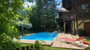Ett trädäck med en pool, omgivet av träd och en träbyggnad med en balkong.