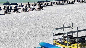 Une plage bordée de rangées de chaises longues et de parasols, avec des kayaks et un poste de surveillance pour les sauveteurs.