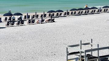 A beach with rows of sun loungers and umbrellas, kayaks, and a lifeguard stand.