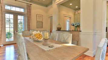 A dining area with a wooden table, a bowl of lemons, a candle, and a vase of flowers.