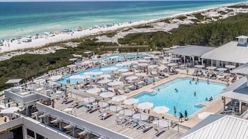 A resort with multiple swimming pools, beach access, and a covered area with lounge chairs and umbrellas.