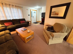 Ein Wohnzimmer mit einer Couch, einem Sessel, einem Couchtisch und einem Fernseher.