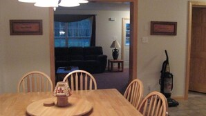 A dining area with a wooden table and chairs, a small decorative item on the table, and a vacuum cleaner in the background. - Sunday River Rental (Bethel)